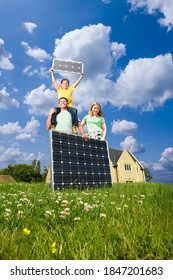 A Low Angle View Of A Happy Family Holding Solar Panels While Standing Out The House On Green Grass Field