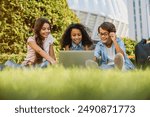 Low angle view of happy little preteen school children kids using digital wireless gadgets laptop with backpacks looking at screen sitting at the grass park outdoors doing home tasks project together