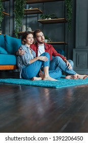 Low Angle View Of Happy Man Hugging Attractive Woman While Sitting On Carpet In Living Room 