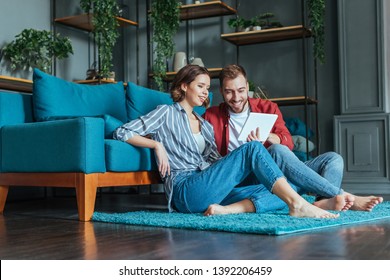 Low Angle View Of Happy Man And Woman Looking At Digital Tablet In Living Room 