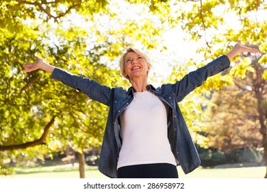 Low Angle View Of Happy Mid Age Woman With Arms Outstretched Outdoors