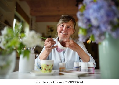 Low Angle View Of Happy Senior Artist Woman Painting Cermaic Cup, Artcraft Concept.