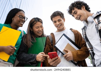 Low angle view of happy young college student friends using mobile phone. Multiracial teenagers using smartphone laughing together outdoor. Youth lifestyle and social media addiction concept. - Powered by Shutterstock