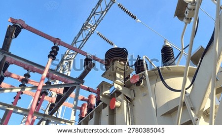 Low angle view of a high voltage power transformer and porcelain insulators at an electrical substation against a clear blue sky. Industrial energy distribution and electricity transmission infrastructure.