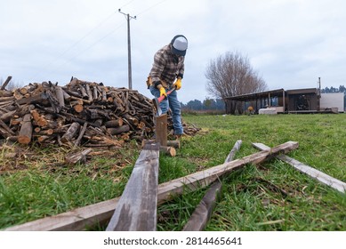 Low angle view of a hispanic man splitting a log with an axe next to a large firewood pile