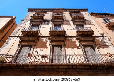 Low angle view of a historic weathered building facade with multiple ornate iron balconies and potted plants in Bosa, Sardinia, Italy