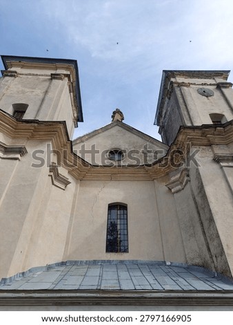 Low angle view of the historical Baroque style Roman Catholic Church of the Annunciation in Sydoriv village, Ternopil region, Ukraine. Impressive damaged stone facade with twin towers and a statue on top against a cloudy sky. Ancient religious heritage architecture