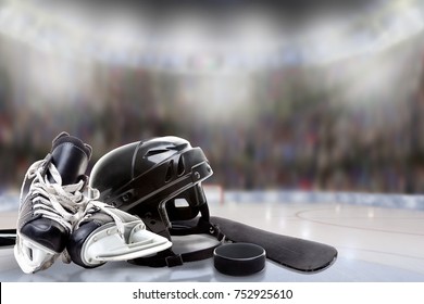 Low angle view of hockey helmet, skates; stick and puck on ice with deliberate shallow depth of field on brightly lit stadium background and copy space.