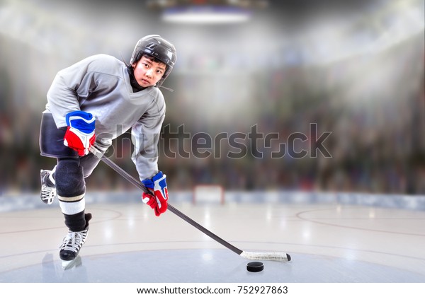 Low angle view of hockey player handling\
puck on ice with sports arena full of fans in the stands and copy\
space. Shallow depth of field on\
background.