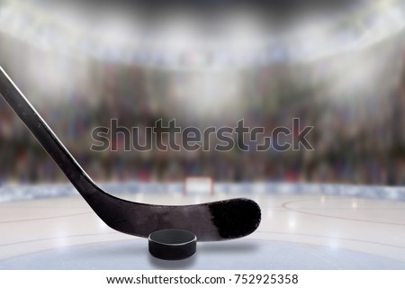 Low angle view of hockey stick and puck on ice with deliberate shallow depth of field on brightly lit stadium background and copy space.