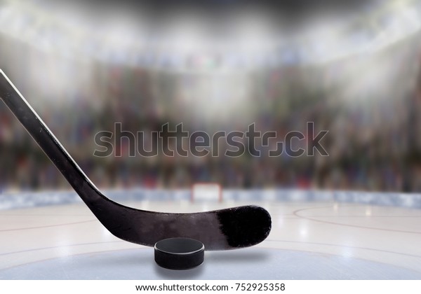 Low angle view of hockey stick and puck on ice\
with deliberate shallow depth of field on brightly lit stadium\
background and copy space.