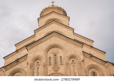 Low angle view of the Holy Trinity Cathedral of Tbilisi (Sameba) at sunset. Majestic Georgian Orthodox architecture with golden stone facade under a dramatic evening sky in Georgia.