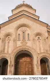 Low angle view of the Holy Trinity Cathedral of Tbilisi (Sameba) at sunset. Majestic Georgian Orthodox architecture with golden stone facade under a dramatic evening sky in Georgia.