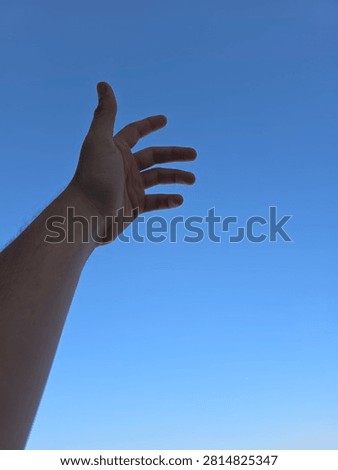 Low angle view of a human hand reaching up towards a clear blue sky