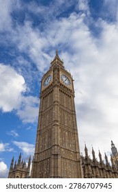 Low angle view of the iconic Big Ben clock tower against a bright blue sky with white clouds in London.