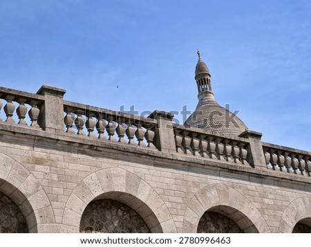 Low angle view of the iconic white travertine dome of the Sacré-Cœur Basilica
in Montmartre, Paris. The architectural detail highlights a classic stone
balustrade and arched masonry in the foreground, leading the eye to the ornate
cupola topped with a cross. Set against a clear blue sky, the shot emphasizes
the Romano-Byzantine style and the historic grandeur of this famous French
landmark.