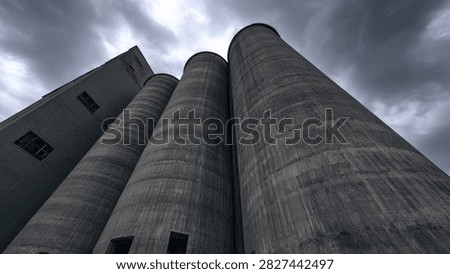 Low angle view of imposing concrete silos against a dark, cloudy sky, conveying a sense of industrial might and impending weather.