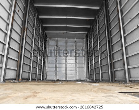 Low angle view inside empty cargo truck with metal walls, plywood floor, and scattered debris. Transportation, logistics, and shipping. Industrial background with perspective and symmetry 
Wide angle shot of empty box truck cargo area with corrugated metal walls and wooden floor. Some trash and dust visible. Transportation, logistics, shipping, and moving industry background.