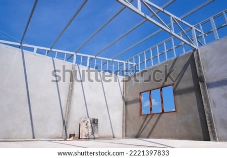 Low angle and view from inside room of concrete wall and shed roof framing structure in under construction against blue sky background