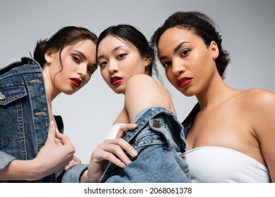 Low angle view of interracial women with red lips looking at camera isolated on grey
