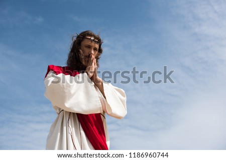 low angle view of Jesus in robe and red sash praying against blue sky