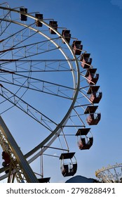 Low angle view of a large Ferris wheel with purple cabins against a clear blue sky in an amusement park