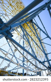 Low angle view of a large ferris wheel with blue and yellow steel beams against a clear sky, showing structure, scale, and modern amusement park design.