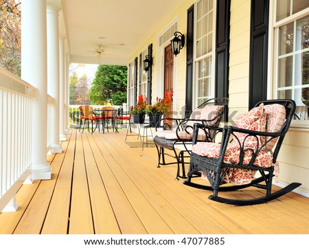 Low angle view of a large front porch with furniture and potted plants. Vertical format.
