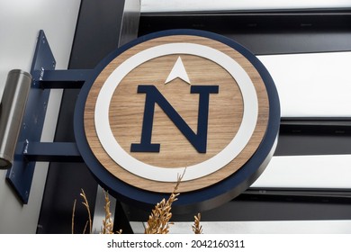 Low Angle View Of A Large N On A Sign, Pointing North In A Large Outdoor Shopping District.