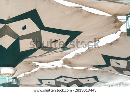Low angle view of large white canvas shade umbrellas decorated with green geometric star patterns against a bright sky