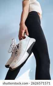 Low angle view of light blue sport shoes held by a young woman showcase modern design. Ideal pair for training, running, or casual outings. Sneakers prioritize comfort and style in home or gym workout