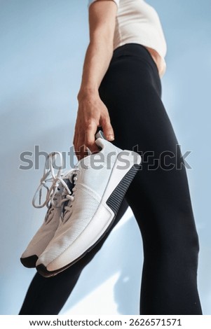 Low angle view of light blue sport shoes held by a young woman showcase modern design. Ideal pair for training, running, or casual outings. Sneakers prioritize comfort and style in home or gym workout