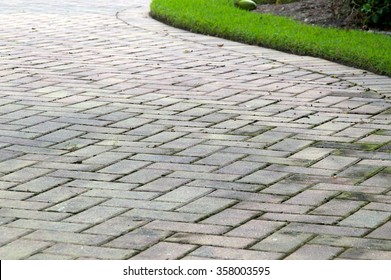Low angle view of  light colored rectangular brick pavers in alternating pattern edged with grass.