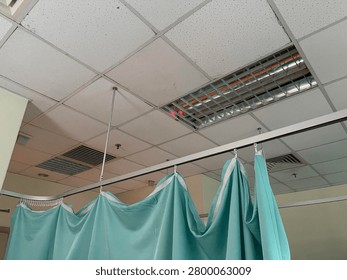 Low angle view of light green medical privacy curtains hanging from a ceiling track inside a hospital ward or clinic examination room.
