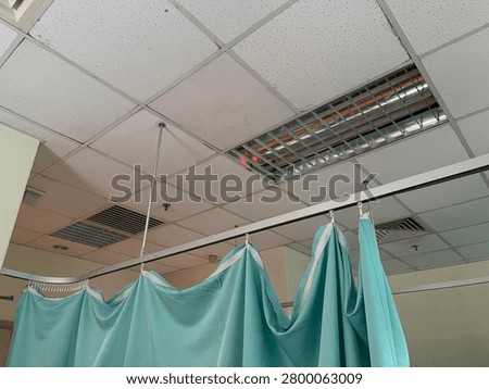 Low angle view of light green medical privacy curtains hanging from a ceiling track inside a hospital ward or clinic examination room.