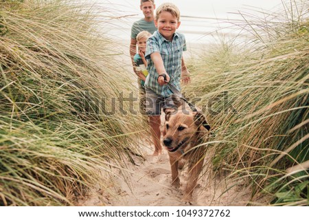 Low angle view of a little boy and his family walking the dog through the sand dunes. 