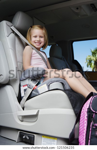 Low angle view of little schoolgirl safely buckled\
into booster seat