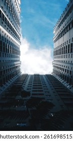 A low angle view looking up between two tall skyscrapers towards a bright blue sky with some clouds. 