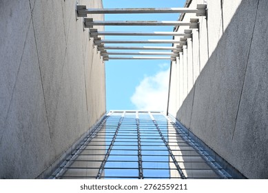 Low angle view looking up between concrete walls at modern glass building and blue sky with white clouds.