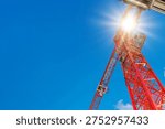 Low angle view looking up at a bright red construction crane structure and boom standing out against a clear blue sky with the sun.
