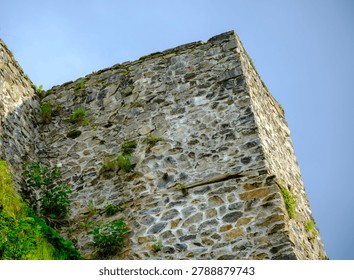 Low angle view looking up at the corner of an imposing medieval stone fortress wall decorated with patches of moss.