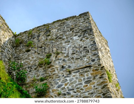 Low angle view looking up at the corner of an imposing medieval stone fortress wall decorated with patches of moss.
