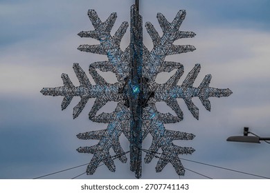 A low angle view looking up at the giant snowflake hanging over the intersection of 57th Street and Fifth Avenue in NYC on a cloudy day.