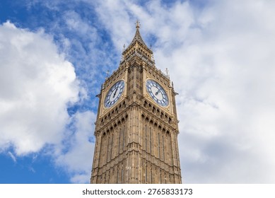 Low angle view looking up at the iconic Big Ben clock face and Elizabeth Tower against a bright blue sky with white clouds in London, United Kingdom.