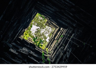 Low angle view looking up inside ancient stone tower square opening sky green trees sunlight perspective architecture ruins mystic atmosphere dungeon prison concept geometric frame