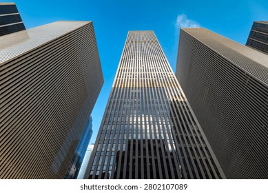 Low angle view looking up at massive corporate office skyscrapers rising high along Avenue of the Americas in New York City.