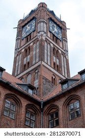 Low angle view looking up at a medieval red brick clock tower from an inner courtyard, showing corner building walls, glass windows, and gold Roman numeral clocks.