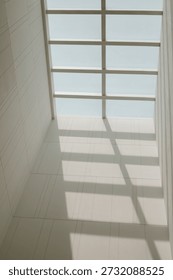 A low angle view looking up at a modern glass skylight grid casting strong geometric lines and shadows on a clean white wall interior during the day.
