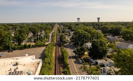 A low angle view looking straight down train tracks with green trees on either side. The tracks run through a suburban neighborhood on a sunny day on Long Island in NY. Shot with a drone camera.