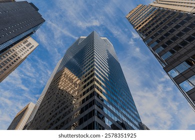 A low angle view, looking up at tall skyscrapers in New York City on a sunny day with blue skies and some white clouds.